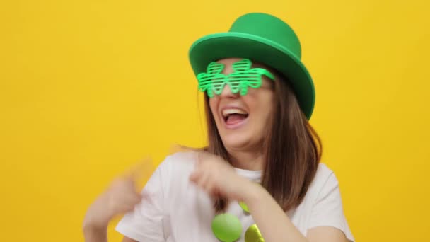 喜びを表現するプロモーションテキストのコピースペースを指す黄色の背景の上に隔離された緑色の帽子を身に着けている笑顔で陽気な女性 — ストック動画