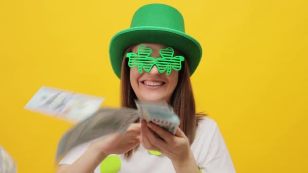 幸せな陽気な女性 Leprechaun パーティーの緑の帽子を着用 黄色の背景に隔離された 大きな利益を楽しむドル紙幣を投げる ホリデーのお祝いのためのたくさんのお金があります — ストック動画
