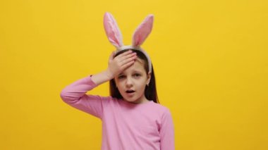 Sarı arka planda duran pembe tavşan kulaklığı takan üzgün küçük kız facepalm hareketi yaparken önemli bir şey unuttu.