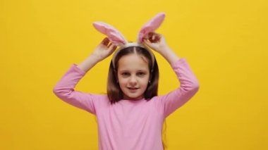 Sarı arka planda dikilmiş pembe tavşan kulaklığı takan komik küçük kız Paskalya bayramını kutluyor ve kutlama için kostümüne hayran.