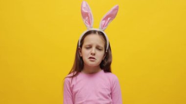Mutsuz üzgün üzgün küçük kız pembe tavşan kulaklığı takıyor sarı arka planda izole bir şekilde duruyor negatif duygularla ağlıyor ve alınıyor.