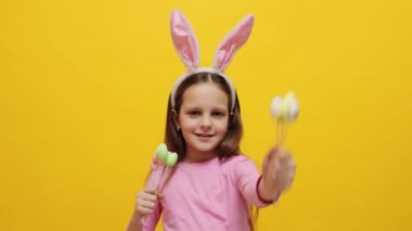 Gülümseyen küçük kız pembe tavşan kulaklığı takıyor elinde pop kekleri var sarı arka planda izole edilmiş poz veriyor lezzetli tatlılar sunuyor