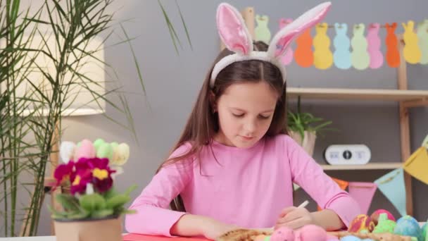 可爱的棕色头发的小女孩戴着兔子耳朵头带制作复活节贺卡 卡片上有艺术创作的材料 为假期准备惊喜 — 图库视频影像