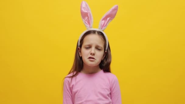 不幸な悲しいことに ピンクのバニーの耳のヘッドバンドを着用した小さな少女は 悪い気分と怒っている否定的な感情で泣いて黄色の背景の上に隔離されています — ストック動画