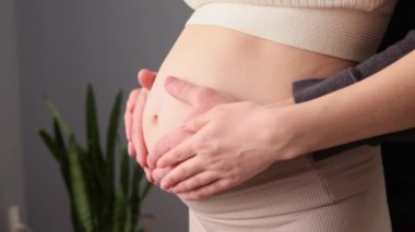 Hamile karnında elleri olan tanınmaz bir anne ve baba. Birbirlerine poz veriyorlar. Müstakbel çocuklarına sevgi ve şefkat gösteriyorlar.