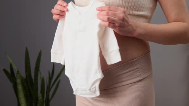 Piękna Nierozpoznawalna Kobieta Ciąży Beżowym Ubraniu Trzymająca Biały Kombinezon Dziecięcy — Wideo stockowe