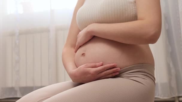 期待着母亲关心她的健康和幸福 子宫里生长着新生命 无法辨认的孕妇坐在地板上摸着肚子 — 图库视频影像
