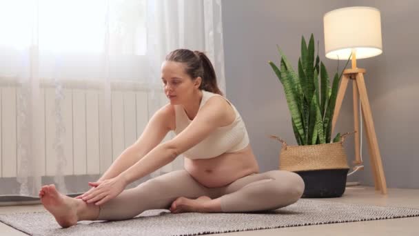 怀孕期间的普拉提和体操 穿着米黄色上衣和腿的快乐的孕妇在轻便的客厅里做家庭运动 以增进健康 — 图库视频影像
