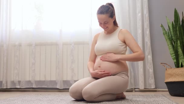 自宅での妊娠の幸せと喜び 妊娠中の女性は 母性への旅を受け入れる 彼女の腹に触れる床に座っている美しい妊婦 — ストック動画