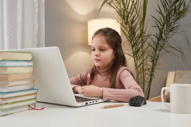 Çevrimiçi öğrenme kaynakları. Çocuk dijital eğitimi. İnternet tabanlı eğitim. Evde otururken dizüstü bilgisayar kullanarak konsantre olmuş küçük kız.