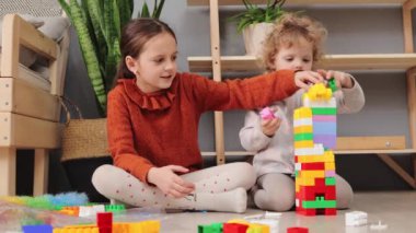 Çocuğun yaratıcı yapısı. Bebeğin renkli blok oyunu bu. Çocuk gelişim binası. Sevimli küçük kız kardeşler oturma odasında çok renkli inşaatçılarla oynuyorlar.