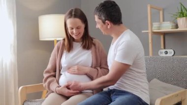 Gelecekteki sıcak aile ilişkileri esmer adam ve hamile karısı birlikte koltukta oturup iletişimin tadını çıkarıyor ve karnını okşayan genç çift bebek bekliyor.
