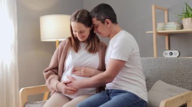 Hamile karısıyla birlikte kanepede oturup birbirlerinin dostluğunun tadını çıkarıyorlar. Karnı nazikçe okşuyorlar. Çiftler, bebeklerinin sıcak ve sevgi dolu bir ilişki kurmalarını dört gözle bekliyorlar.