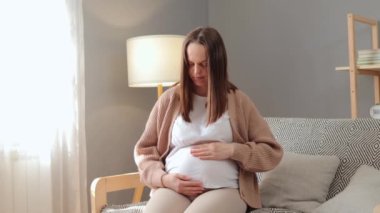 Üzgün hayal kırıklığına uğramış Kafkasyalı hamile kadın koltukta oturuyor ve depresyonda. Hamilelik boyunca yalnız. Karnını okşayıp iç çekiyor.