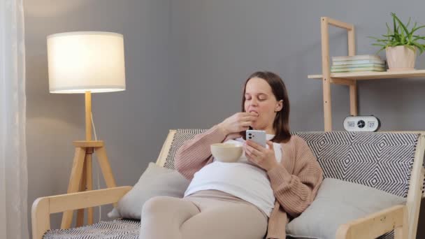 그녀의 거실에서 휴식을 취하면서 건강한 간식을 즐기는 그녀의 전화를 가정에서 — 비디오