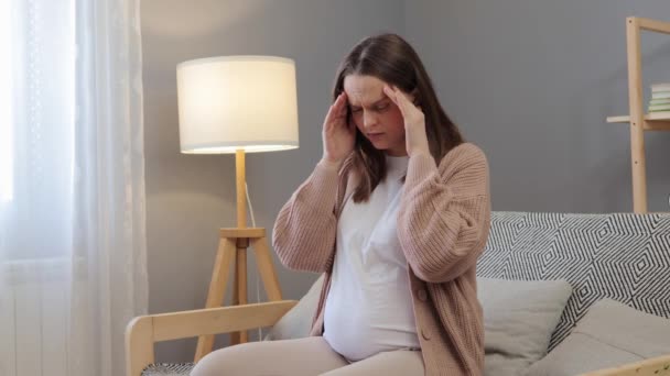 生病的孕妇头疼得厉害 她坐在客厅里给自己痛苦的太阳穴按摩 沙发上有偏头痛症状的孕妇 — 图库视频影像