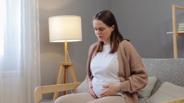 年轻的黑发孕妇在家中感到不适 在抚摸肚子痛的同时 面带微笑 感到肚子痛 — 图库视频影像