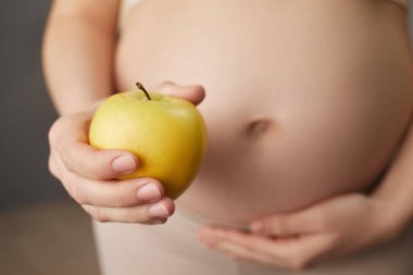 Kimliği belirsiz hamile bir kadın organik sarı elma tutuyor. Hamilelik boyunca sağlıklı beslenmenin tadını çıkarıyor. Evinde vitamin atıştırması yapan, tanınmayan bir kadın.