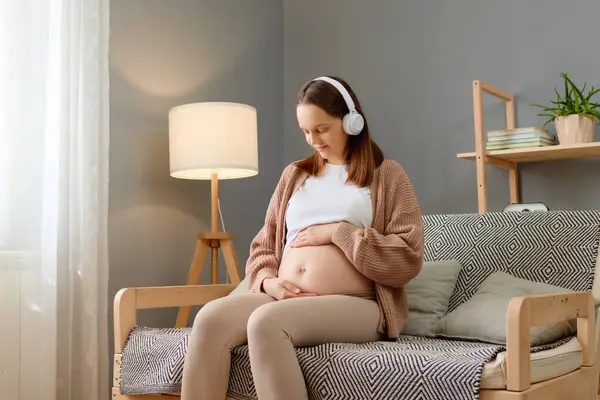 Wanita Cantik Berambut Coklat Duduk Sofa Dengan Headphone Menyentuh Perutnya — Stok Foto