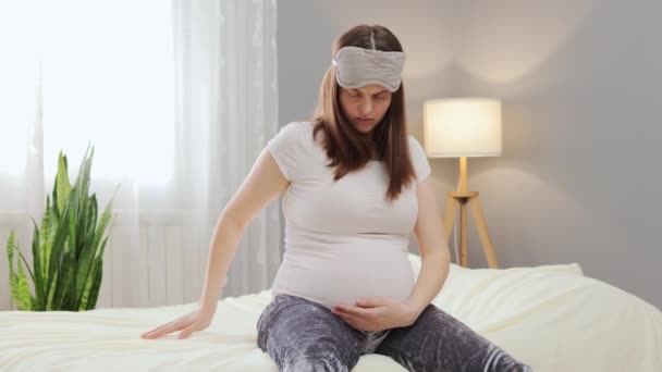 若い美しい妊娠中の女性は ベッドルームのベッドに座って出産を準備する労働収縮の痛みを感じて 彼女の腹をストロッキング神経質に見えます — ストック動画