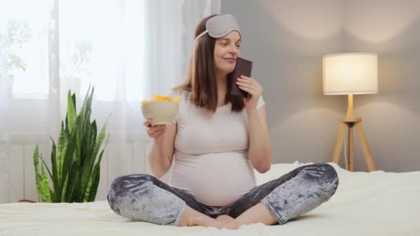 Mujer Embarazada Eligiendo Qué Comer Chocolate Papas Fritas Sentado Cama — Vídeos de Stock