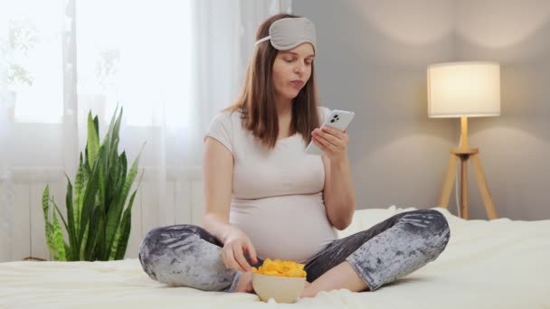 Moderne Gravid Kvinne Som Bruker Smarttelefon Spiser Chips Mens Slapper – stockvideo