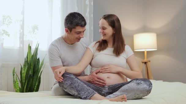 美丽的孕妇和她英俊的丈夫笑着在床上共度时光 男人抚摸着肚子里的婴儿 表达爱意和温存 — 图库视频影像