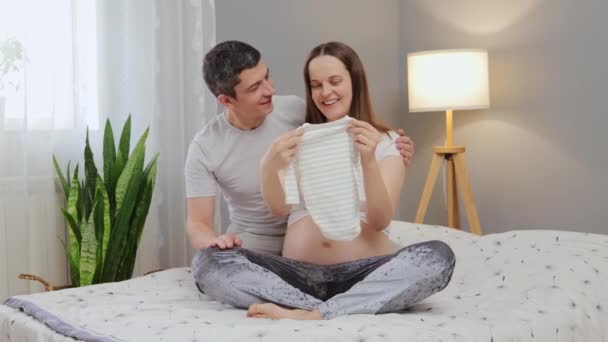 Familjen Häckar Förväntan Gravida Par Sängen Sovrummet Tittar Baby Kläder — Stockvideo