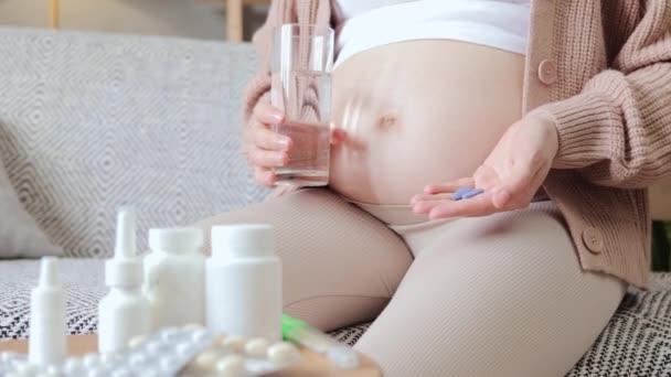 認知できない病気の不健康な妊婦は 自宅でソファーに座って 妊娠中に病気を治療する薬と水のガラスを保持している彼女の裸の腫瘍を示しています — ストック動画