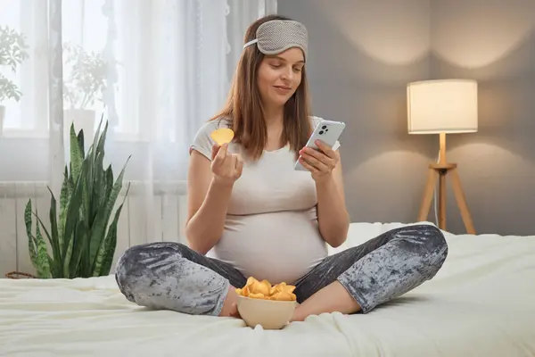 Smiling Pregnant Caucasian Woman Using Smartphone Eating Chips While Relaxing — Stock Photo, Image