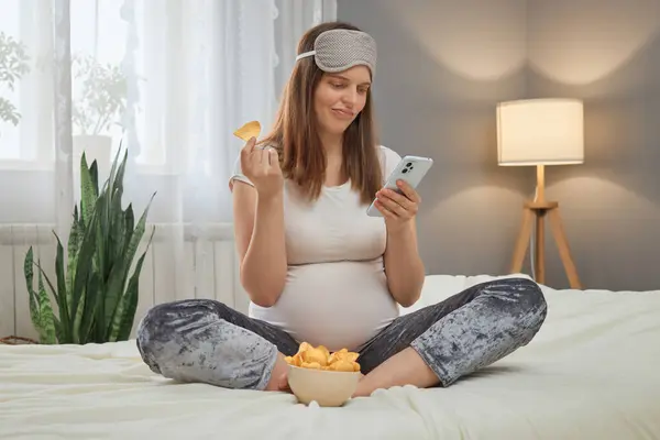 Relaxing Bed Snacks Confused Pregnant Woman Smartphone Hands Eating Chips — Stock Photo, Image