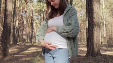 Neşeli Kafkasyalı hamile kadın, yeşilliklerin ve ağaçların arasında sağlıklı ve aktif bir vücut bulmak için bahar günlerinde parkta ya da ormanda vakit geçiriyor.