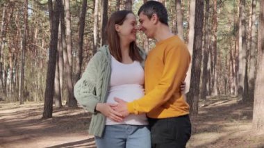 Mutlu, mutlu bir çift, odunların içinde, hamile bir kadına sarılıyorlar. Ormanda ya da parkta dururken, sevgi dolu kocasının karnına dokunmasıyla ormanda güzel doğanın tadını çıkarıyorlar.