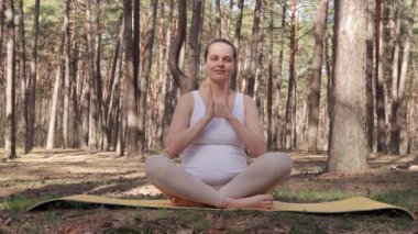 Spor kıyafetleri giyen, pırıl pırıl hamile bir kadın nilüferde oturup sakin bahar ormanlarında meditasyon yapan annelik beklentisiyle yoga yapıyor.