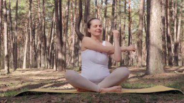 Bahar ormanlarında spor yapan kararlı bir kadın ellerini uzatarak kendisi ve doğmamış çocuğu için sağlığını ve sağlığını geliştiriyor.