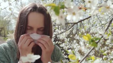 Polen alerjisi. Hasta, genç ve güzel bir kadın çiçek açan kiraz ağacının önünde hapşırıyor. Sağlıksız bir kadın mendil kullanarak alerjik ritüeller geçiriyor.