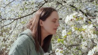 Beyaz kadın, bahçede yürürken güzel kiraz ağacı çiçekleri koklarken mendil kullanarak mevsimlik polen alerjisi çekiyor.