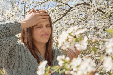 Baharda çiçek açan bahçede acı veren alnına dokunarak mevsimsel alerjiden muzdarip beyaz, kahverengi saçlı kadın alerjisi.