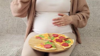 Hamile abur cubur aşığı. Sağlıksız beslenme aldatmacası. Tanımlanamayan hamile bir bayan pizzanın tadını çıkarıyor. Lezzetli bir dilim pizzanın karnını okşuyor.