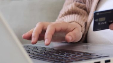 Evde dizüstü bilgisayar ve kredi kartıyla çalışan hamile bir kadın online alışveriş için ödeme yapan bankacılık uygulamasını kullanarak klavyede yazı yazıyor.