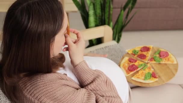 准妈妈满足了她的渴望 享受着片刻的放松 吃着美味的披萨 躺在沙发上 怀孕的女性沉溺在披萨里 — 图库视频影像