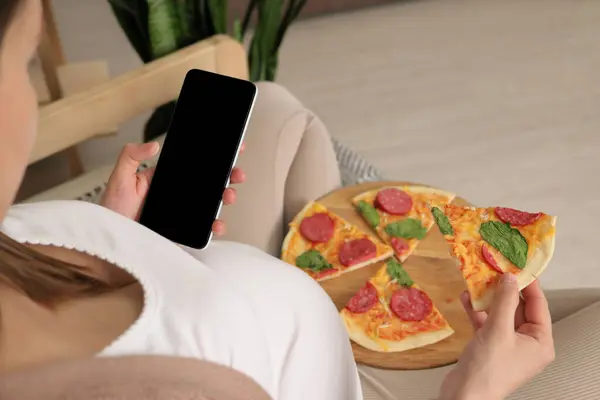 Unrecognizable pregnant woman enjoying pizza holding tasty slice and smartphone with empty display copy space for advertisement empty area for promotion
