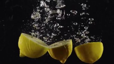 Arka planda kabarcıklar olan limon yarıları düşüyor ya da berrak suya düşüyor