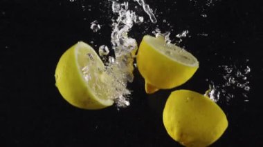 Suyun altına düşen limon yarımları ve siyah arka planda izole edilmiş su damlaları.