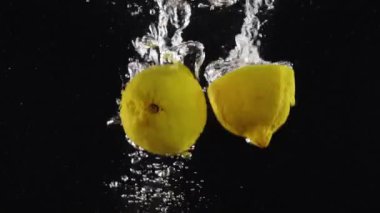 İki tane taze limon suya batıyor ve siyah arkaplana çarpıyor.