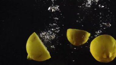 Limon, siyah arka planda izole edilmiş su ve hava kabarcıklarıyla suya düştü.