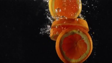 Bir grup taze organik portakal, siyah arkaplana sıçramış bir şekilde suya düşüyor.