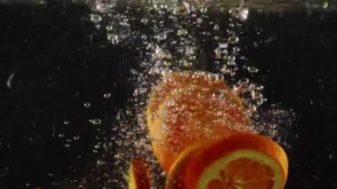 Suda yüzen portakal dilimleri ve siyah arka planda hava kabarcıkları.