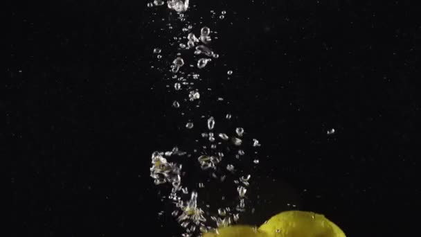 Ζουμερά Λεμόνια Που Πέφτουν Στο Νερό Φυσαλίδες Απομονωμένες Μαύρο Φόντο — Αρχείο Βίντεο