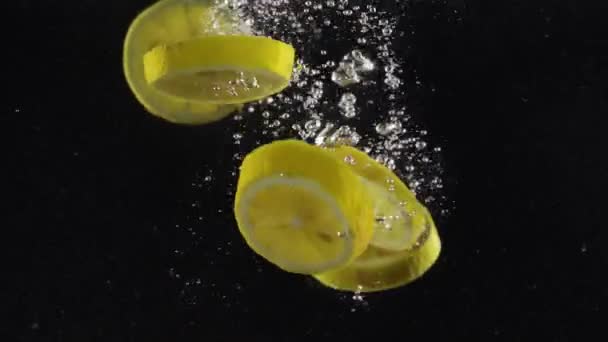 黒い背景に隔離されたスプラッシュと空気泡で水に落としたレモンのスライス — ストック動画
